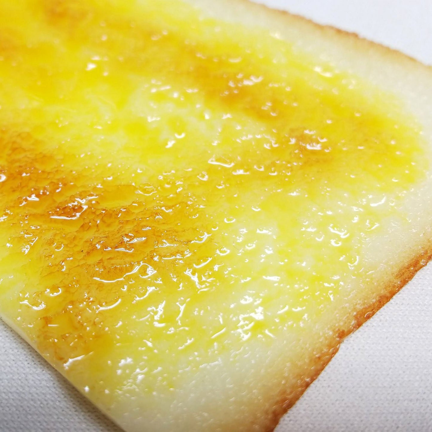 Macro close-up of a glossy, golden-browned buttered toast bookmark with realistic melted butter texture on the surface.