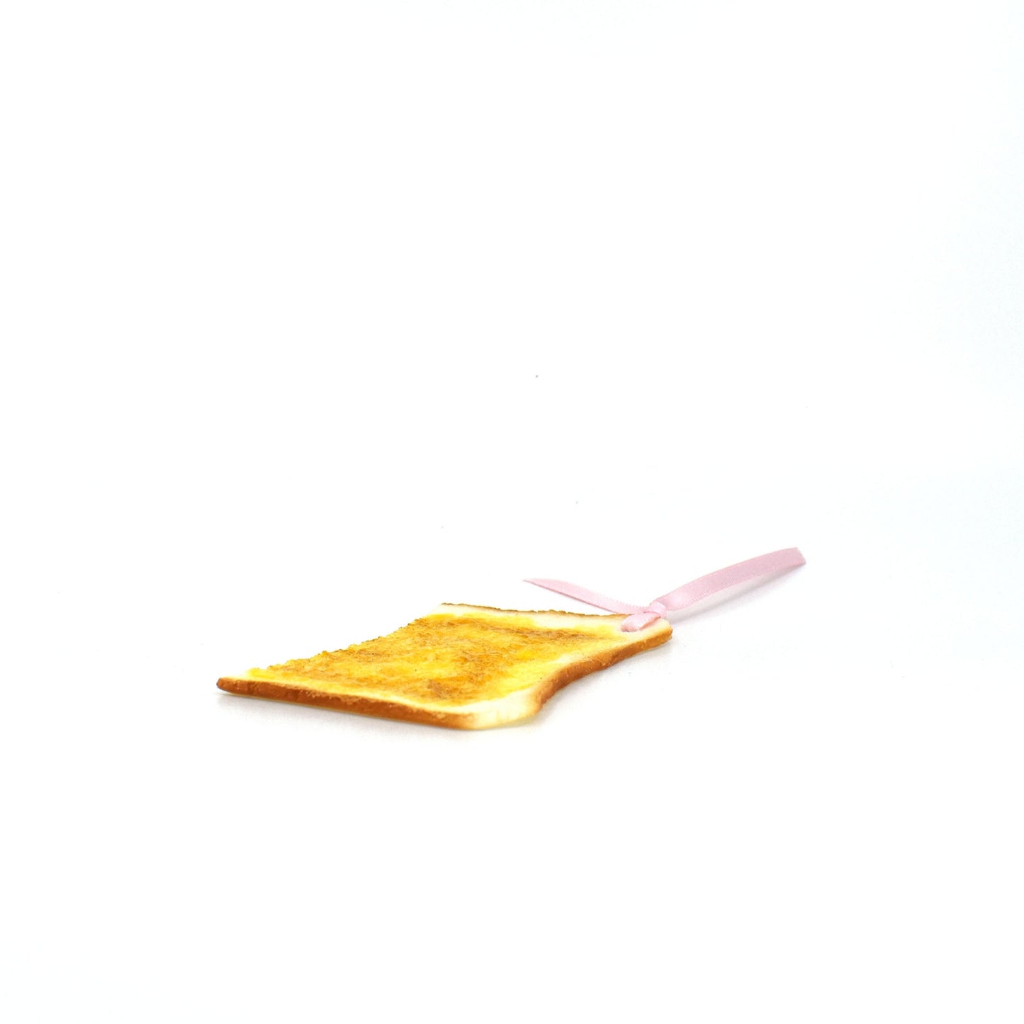 Side view of a realistic buttered toast bookmark with a glossy texture and a soft pink ribbon, set against a clean white background.