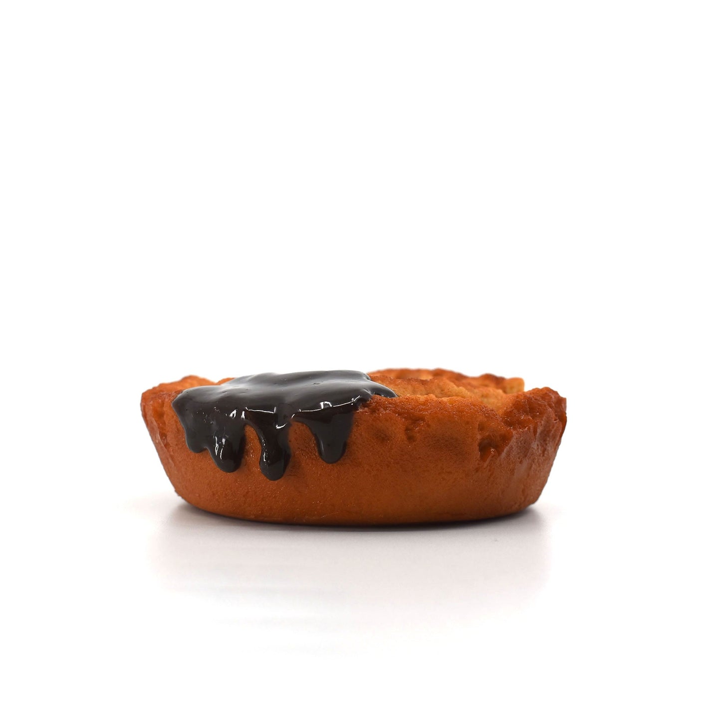 Side view of a realistic donut-shaped phone stand with glossy chocolate glaze dripping down the edge, placed on a white surface.