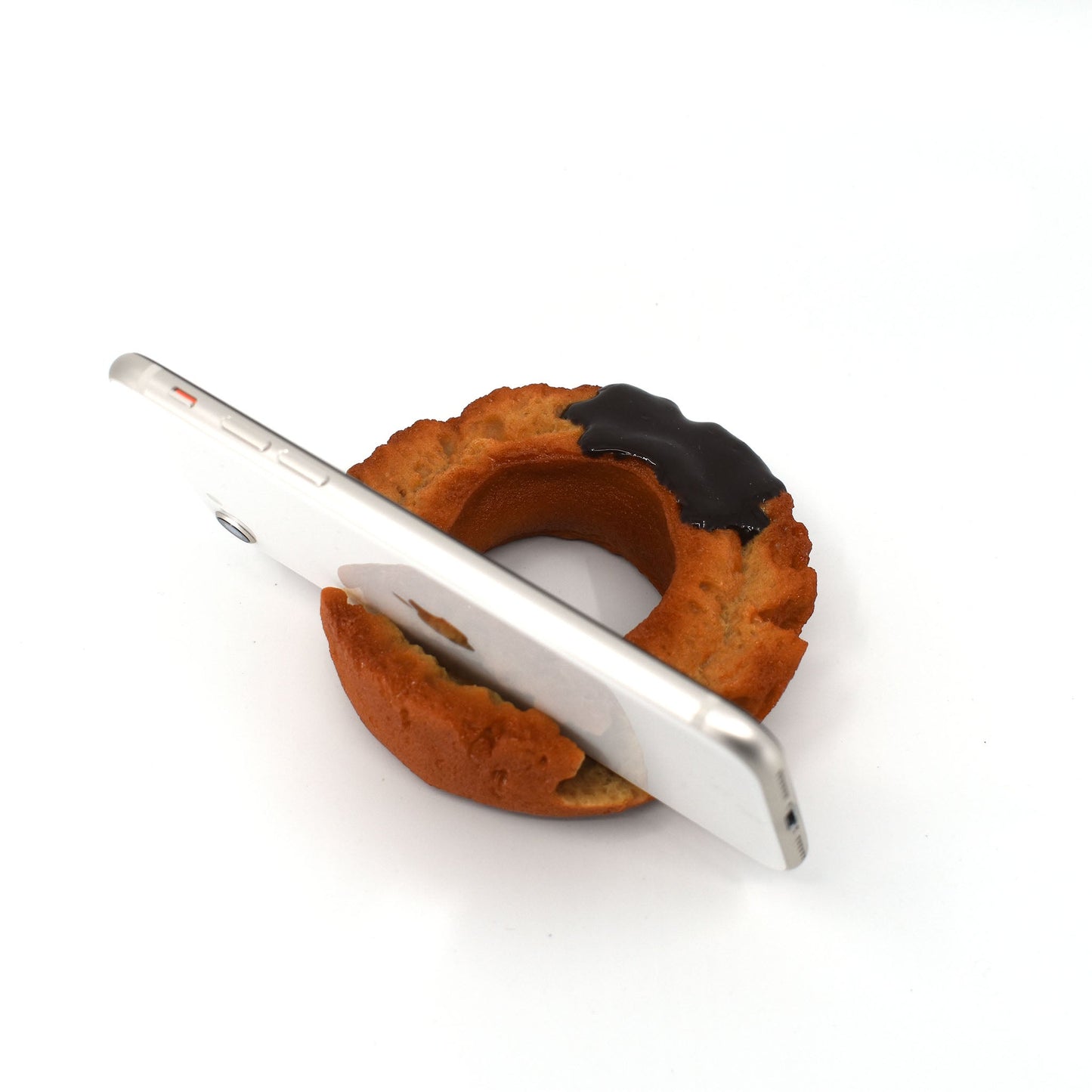 Angled view of a smartphone propped upright in a realistic chocolate donut-shaped stand, mimicking a half-eaten pastry with glossy glaze detail.