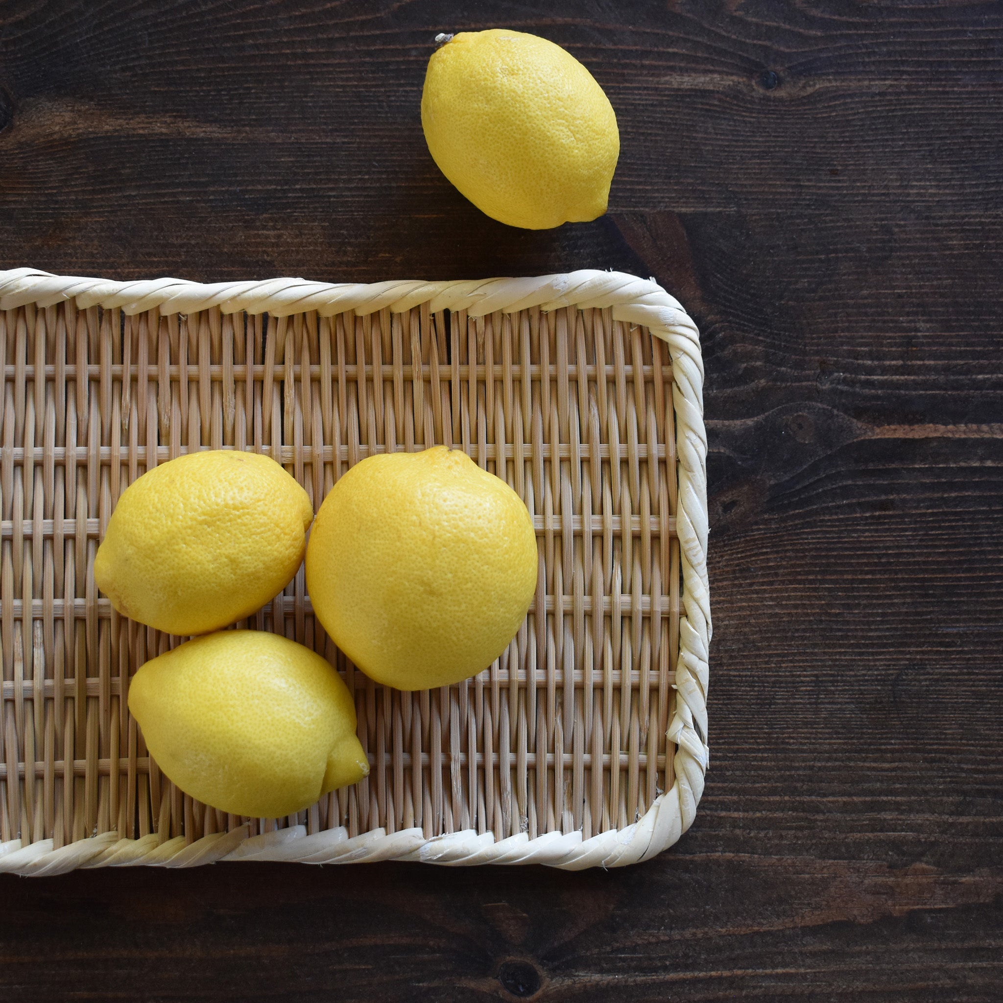 Rectangular handwoven bamboo tray displayed on a dark wooden table with fresh lemons placed on top, showcasing its natural texture and versatility.