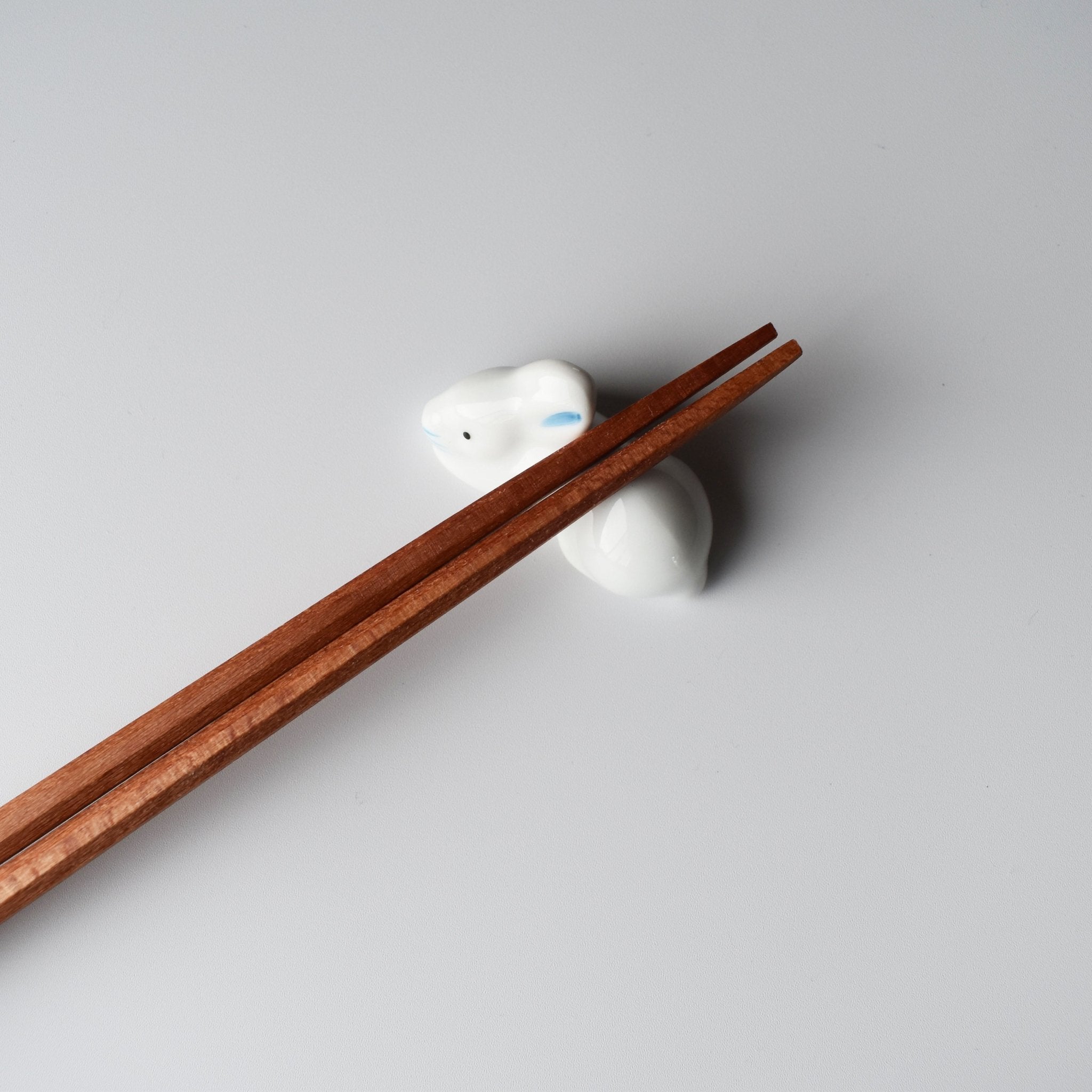 Peach wood chopsticks resting on a white ceramic rabbit holder