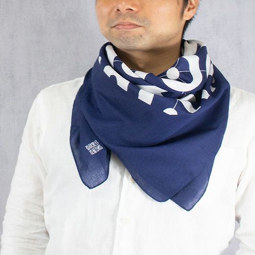 Man wearing a traditional Japanese furoshiki scarf in indigo blue with modern white swirl design, folded into a triangular neck wrap over a white shirt.