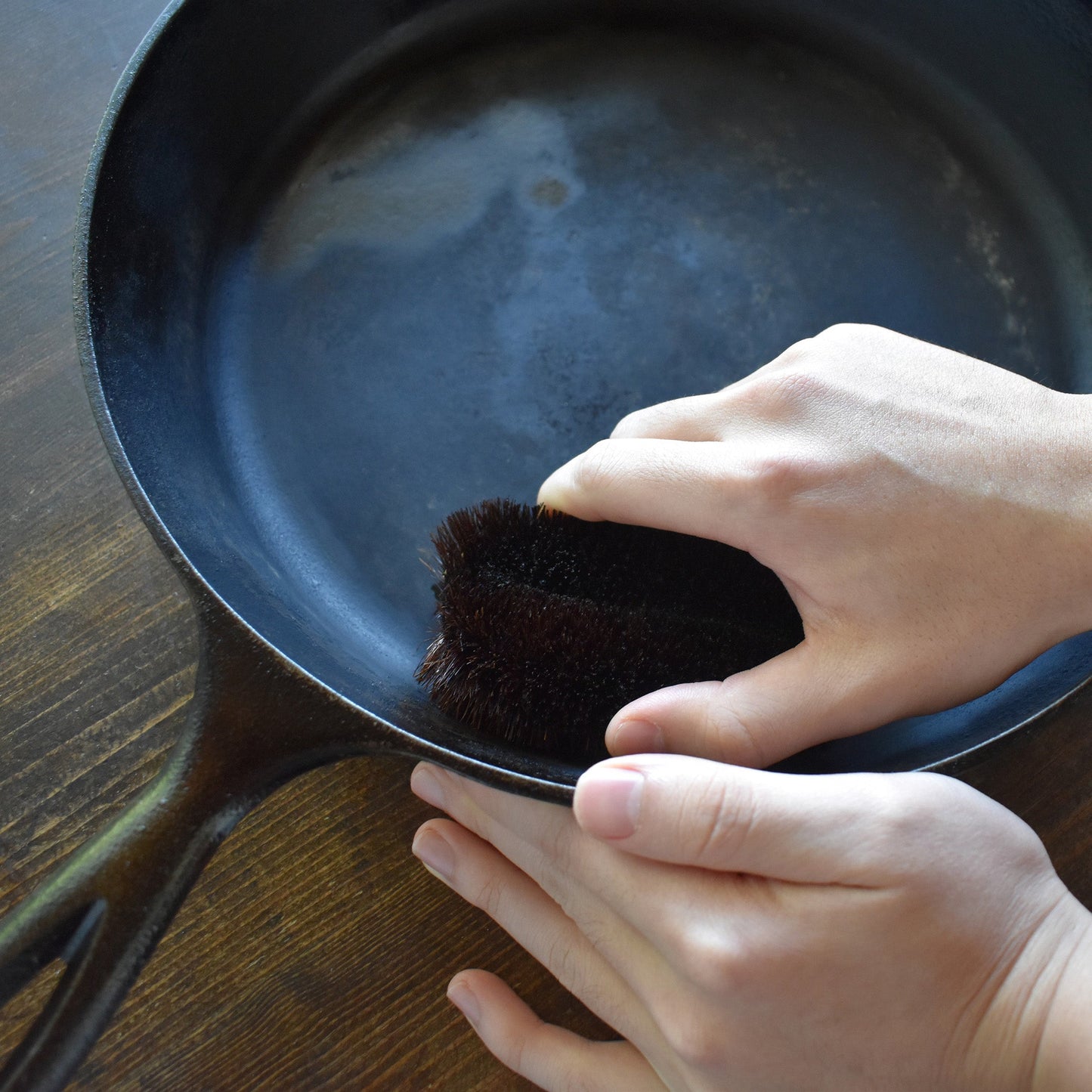 Hand using a shuro tawashi scrubber to clean a cast iron skillet on a wooden surface