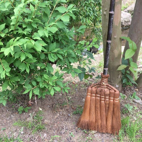 Shojiya Denbei Shuro Broom leaning against a tree in a Japanese garden, showcasing its natural materials and traditional craftsmanship.