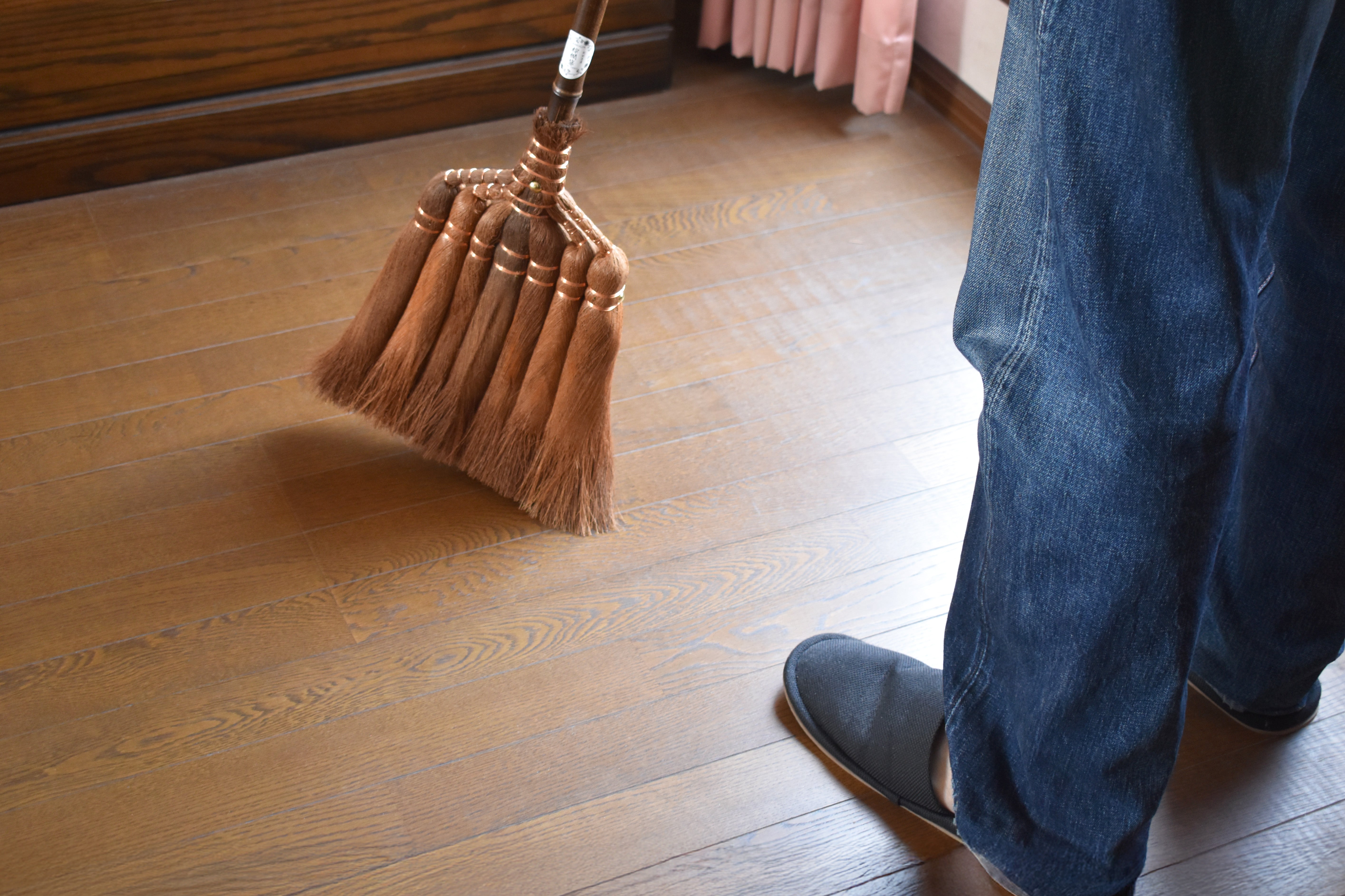Person sweeping a wooden floor with a handcrafted Japanese Shuro broom, a traditional eco-friendly cleaning tool made from palm fibers.