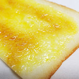 Macro close-up of a glossy, golden-browned buttered toast bookmark with realistic melted butter texture on the surface.
