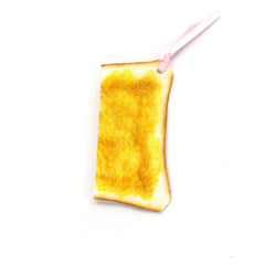 Bookmark shaped like a slice of toast with a shiny golden buttered surface and a pink ribbon loop on a white background.