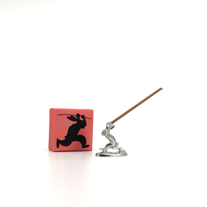 Silver Chōjū-giga rabbit incense holder with a stick of incense, shown beside its red illustrated packaging box.
