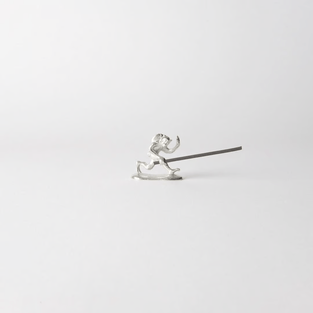 Chōjū-giga monkey-shaped incense holder made from cast tin, holding a lit incense stick in a minimalist white setting – inspired by Japan’s oldest picture scroll.