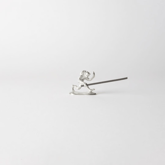 Chōjū-giga monkey-shaped incense holder made from cast tin, holding a lit incense stick in a minimalist white setting – inspired by Japan’s oldest picture scroll.