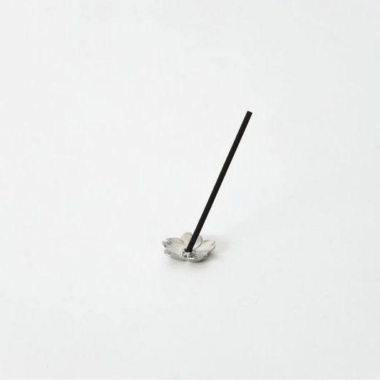 Sakura-shaped pewter incense holder with a stick of incense standing upright in the center, displayed on a white background.