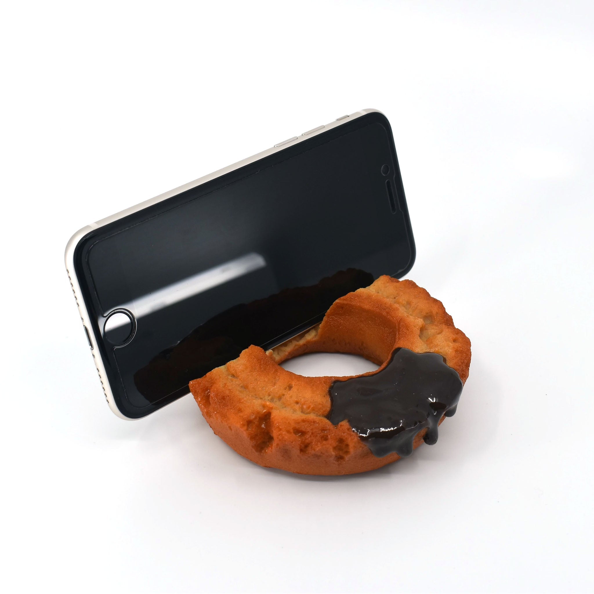 Phone resting securely in a realistic chocolate-glazed donut stand, designed to resemble a half-bitten old-fashioned donut with a glossy topping.