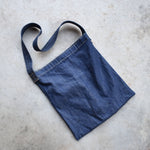 Flat lay of minimalist Japanese denim shoulder bag with wide strap and reinforced stitching, perfect for daily use or travel