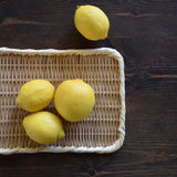 Rectangular handwoven bamboo tray displayed on a dark wooden table with fresh lemons placed on top, showcasing its natural texture and versatility.