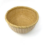 Angled view of a handwoven Japanese bamboo basket with round shape and smooth rim, used for rinsing rice or kitchen storage