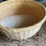 Natural bamboo basket filled with rinsed white rice, placed on a kitchen counter, showcasing traditional Japanese rice washing technique