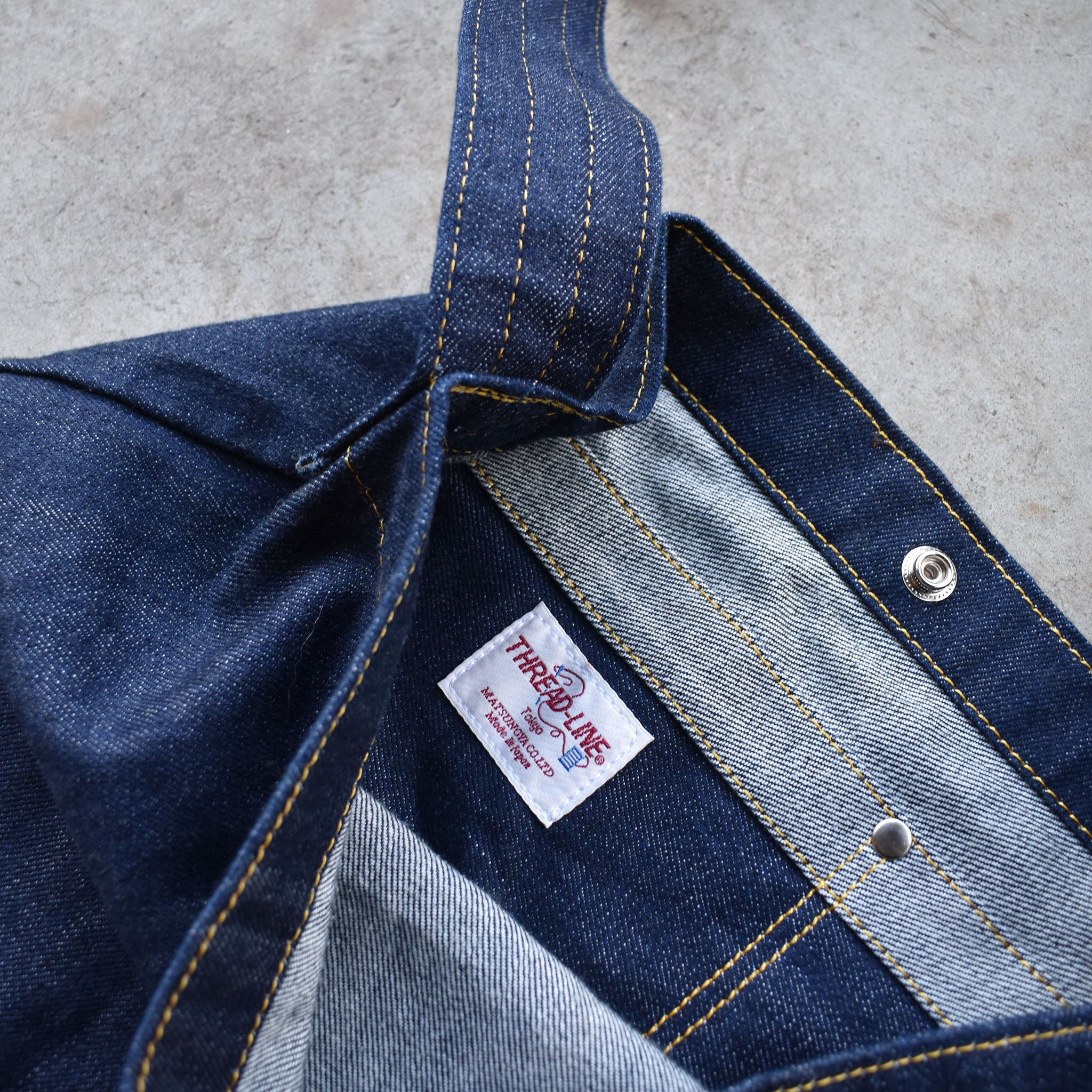 Close-up of Japanese denim shoulder bag interior showing pocket stitching, snap closure, and Three Lake Japan brand label