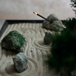 Burning incense stick resting on stone within a miniature Karesansui Zen Garden.