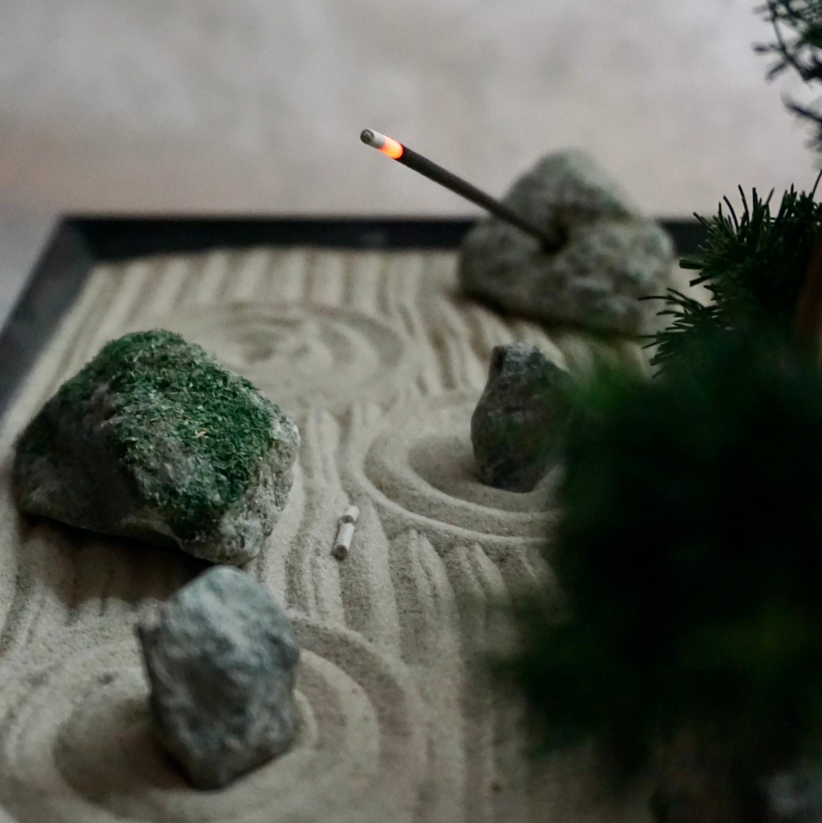 Burning incense stick resting on stone within a miniature Karesansui Zen Garden.