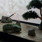 Miniature Zen garden with bonsai and burning incense, representing a Karesansui landscape.