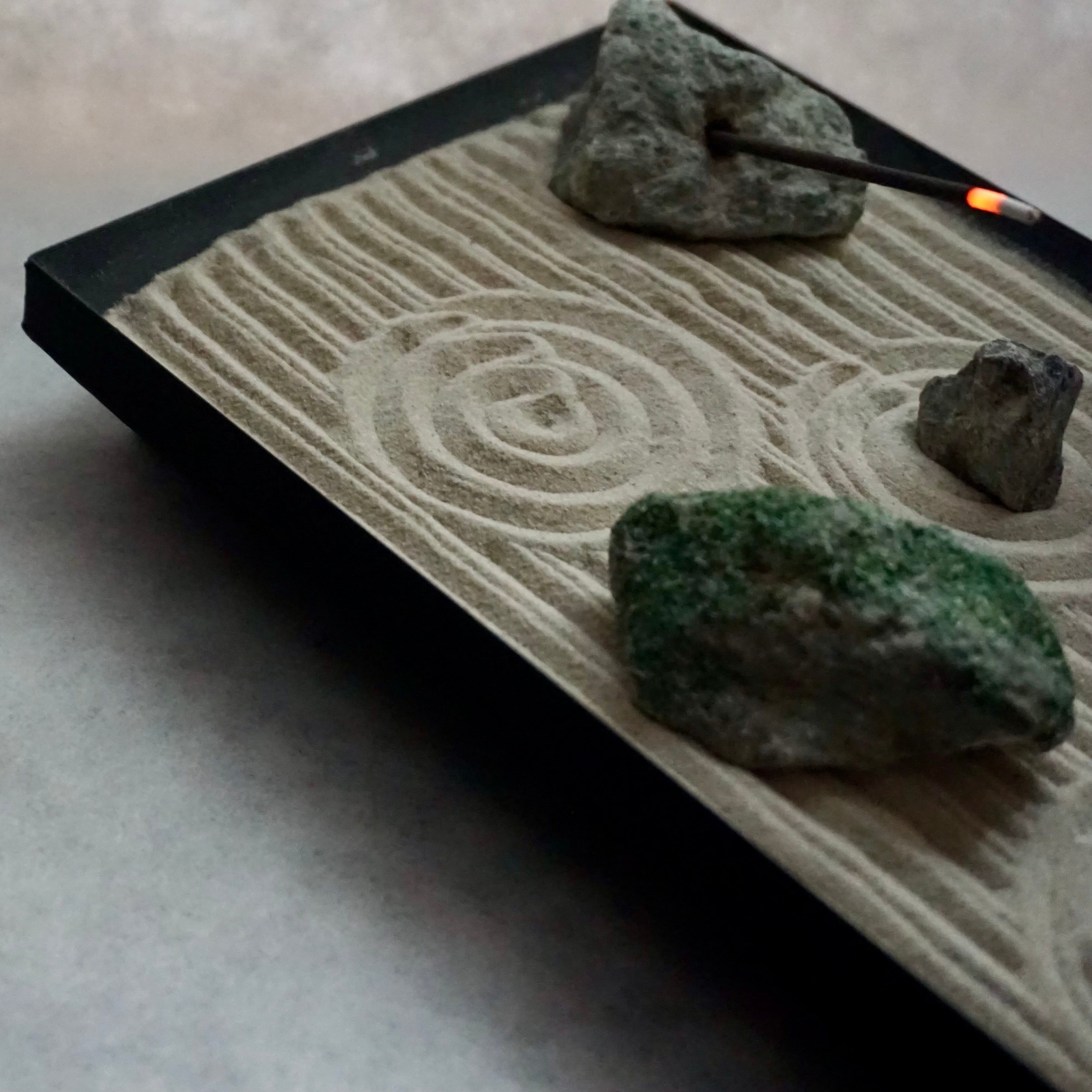 Top view of sand patterns and incense holder stone in a small Zen garden.