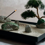 Japanese Karesansui Zen Garden showing sand, moss-style stones, bonsai, and incense stick.