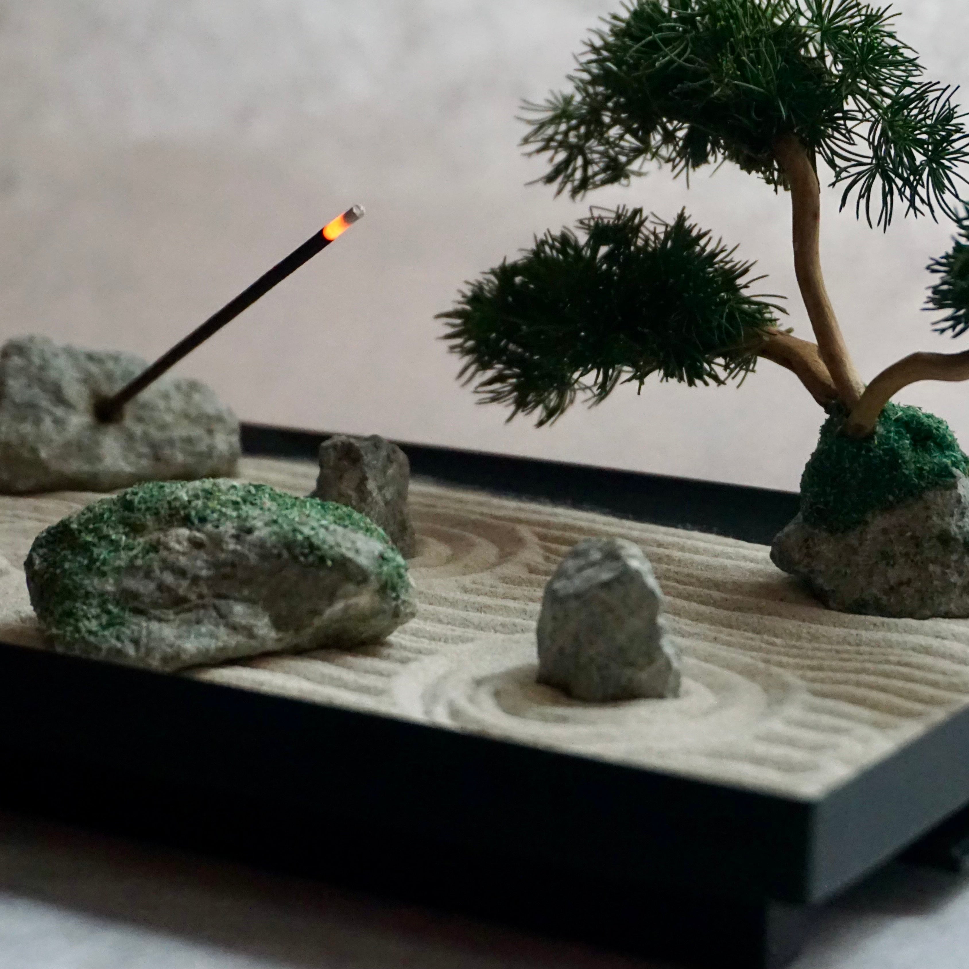 Japanese Karesansui Zen Garden showing sand, moss-style stones, bonsai, and incense stick.