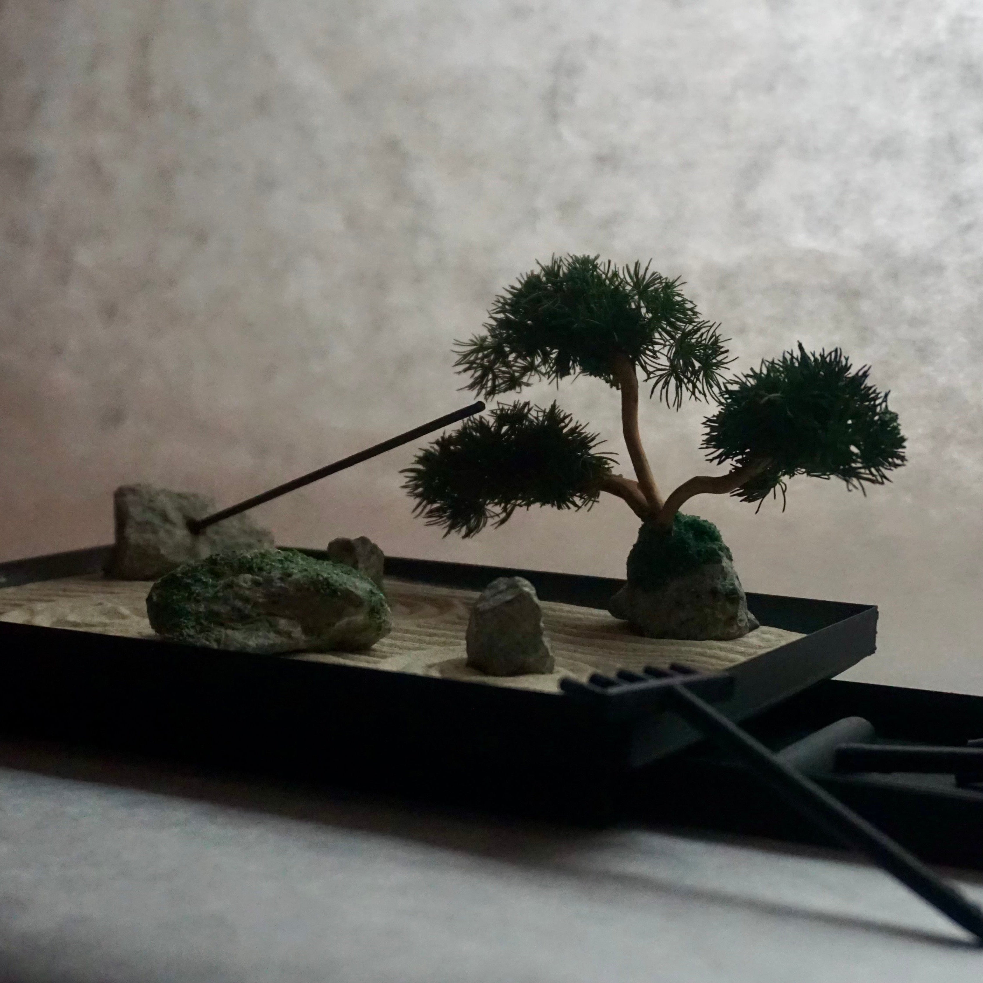 Miniature Karesansui Zen Garden with bonsai tree, burning incense, and bamboo rake.
