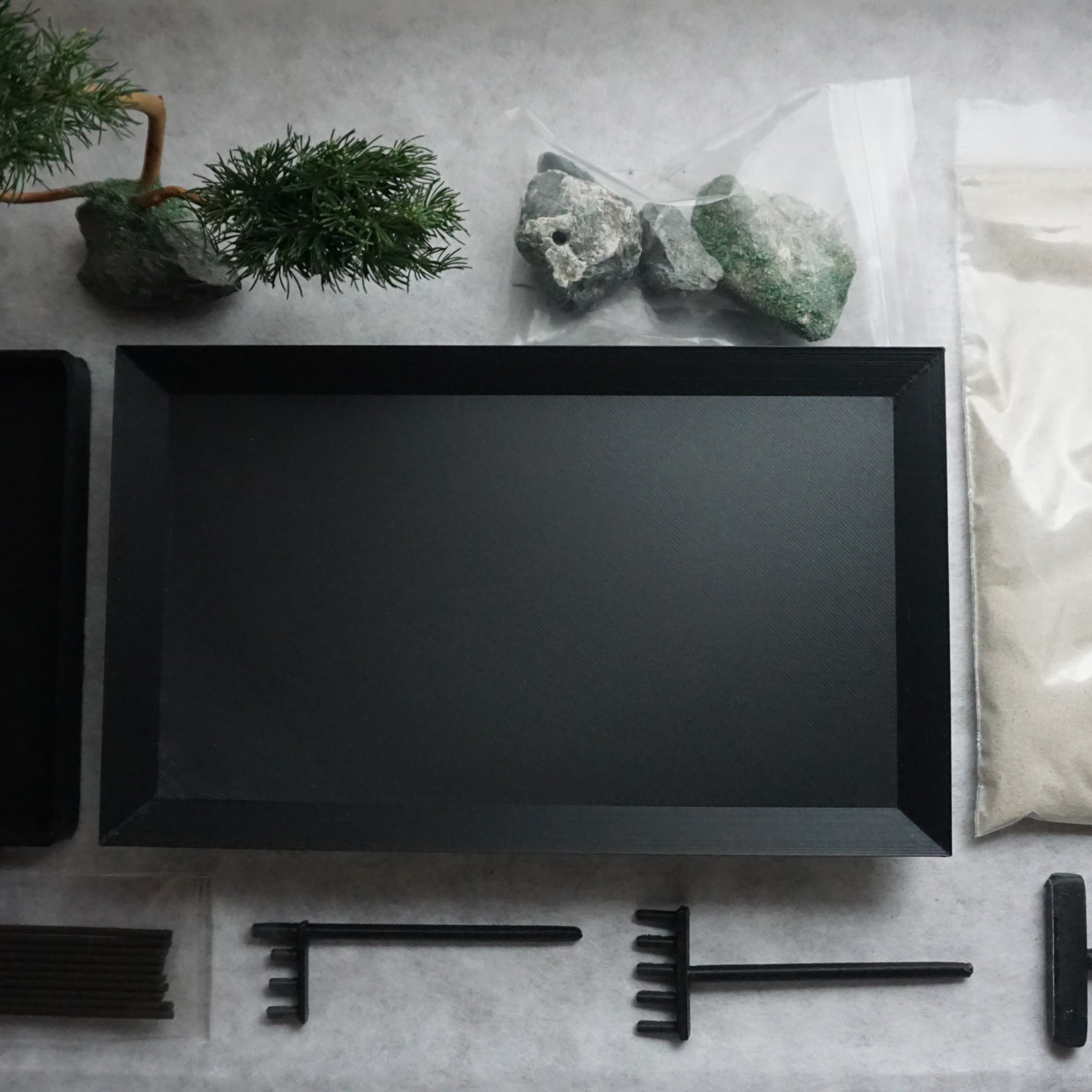 Components of the Karesansui Zen Garden Incense Holder including tray, bonsai, stones, sand, and tools.