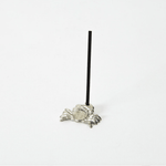 Side view of a silver crab-shaped incense holder with a black incense stick standing upright in the center, placed on a white background.