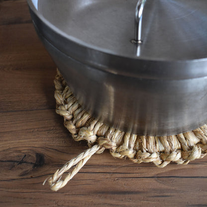 Metal pot resting on a handwoven Japanese straw trivet with hanging loop, placed on a wooden surface, demonstrating heat protection and natural style