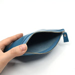 Hand holding open an ocean blue leather pouch with zipper, showing spacious suede-lined interior, ideal for daily carry or accessories.