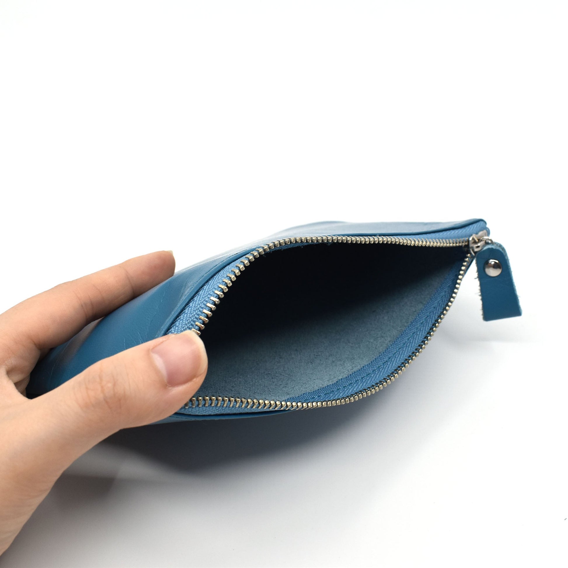 Hand holding open an ocean blue leather pouch with zipper, showing spacious suede-lined interior, ideal for daily carry or accessories.