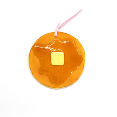 Top-down view of a round pancake-shaped bookmark with glossy syrup and a pat of butter, finished with a pink ribbon loop.