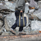 Man walking outdoors holding a rugged Japanese selvage denim tote bag with olive green handles and Thread Line label