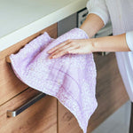 A person wiping a wooden kitchen drawer with a soft lavender Japanese cloth patterned with delicate white cherry blossom petals.