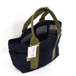 Angled view of compact Japanese selvage denim tote bag with olive webbing handles, visible Thread Line label, and open interior pockets