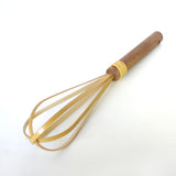 Angled view of a traditional Japanese rice washing whisk made of split bamboo and wood handle, resting on a white background.