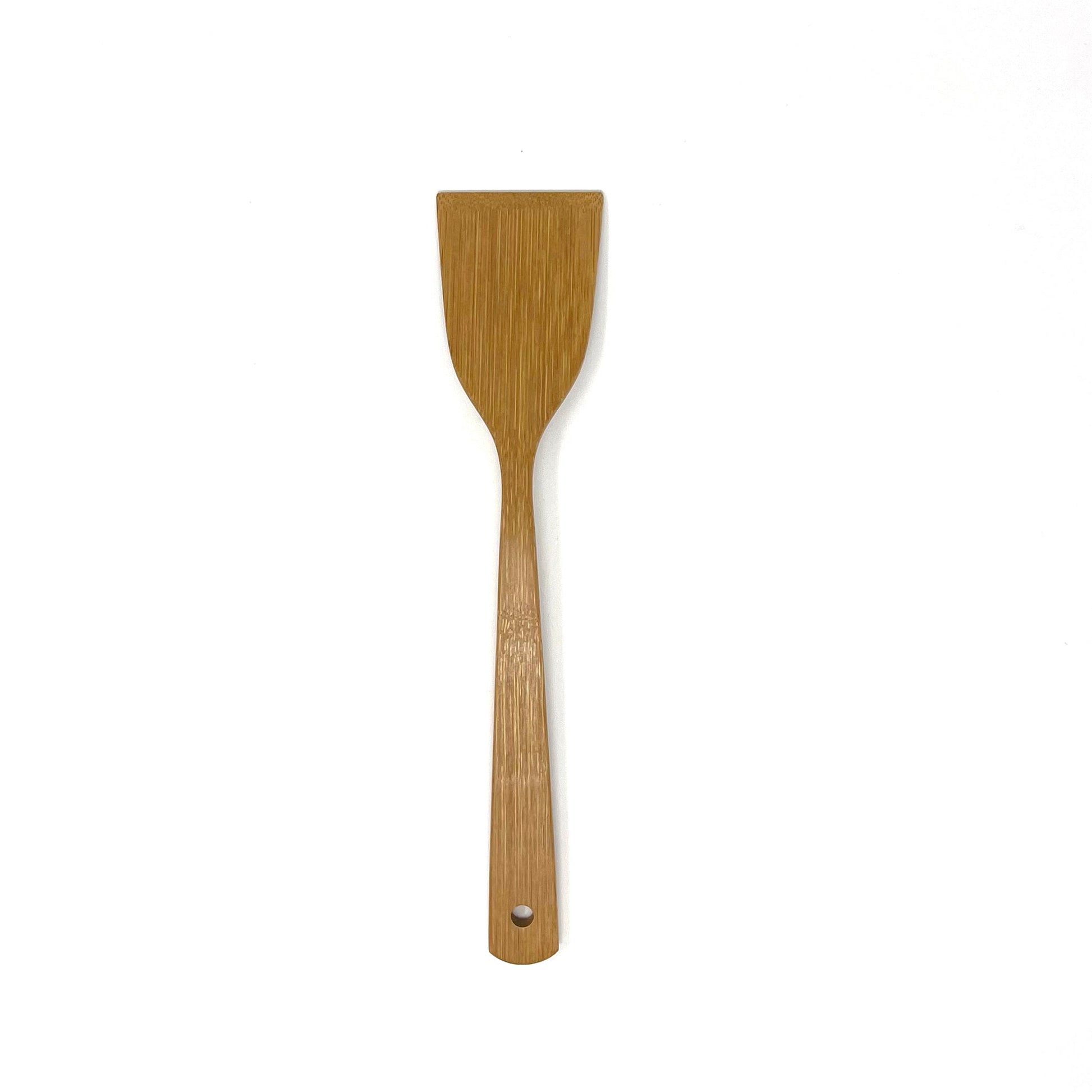 Minimalist bamboo cooking turner photographed against a clean white background, featuring a flat, wide head for flipping and stirring, a gently tapered neck for ergonomic grip, and a small hole at the base of the handle for easy hanging.