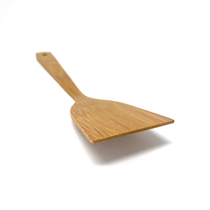 Angled view of a handcrafted bamboo cooking turner, highlighting its flat, wide blade with a beveled edge designed for flipping and stirring food with precision and control.