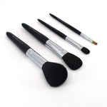 Angled view of four Chikuhodo makeup brushes arranged diagonally on a white surface, featuring sleek black handles, silver ferrules, and soft bristles in varying shapes for face and eye application.