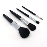 Angled view of four Chikuhodo makeup brushes arranged diagonally on a white surface, featuring sleek black handles, silver ferrules, and soft bristles in varying shapes for face and eye application.