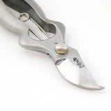 Close-up of Hidehisa stainless garden pruners showing curved blade and engraved logo. 