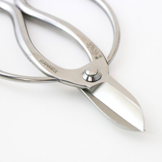 Close-up of Hidehisa stainless steel floral shears highlighting the sharp blade edge and engraved Japanese characters on the polished handle.