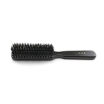 Side profile of a Kanaya medium-stiffness natural bristle hair brush, showcasing densely packed black bristles and a smooth black wooden handle with gold Japanese lettering, placed on a white background.