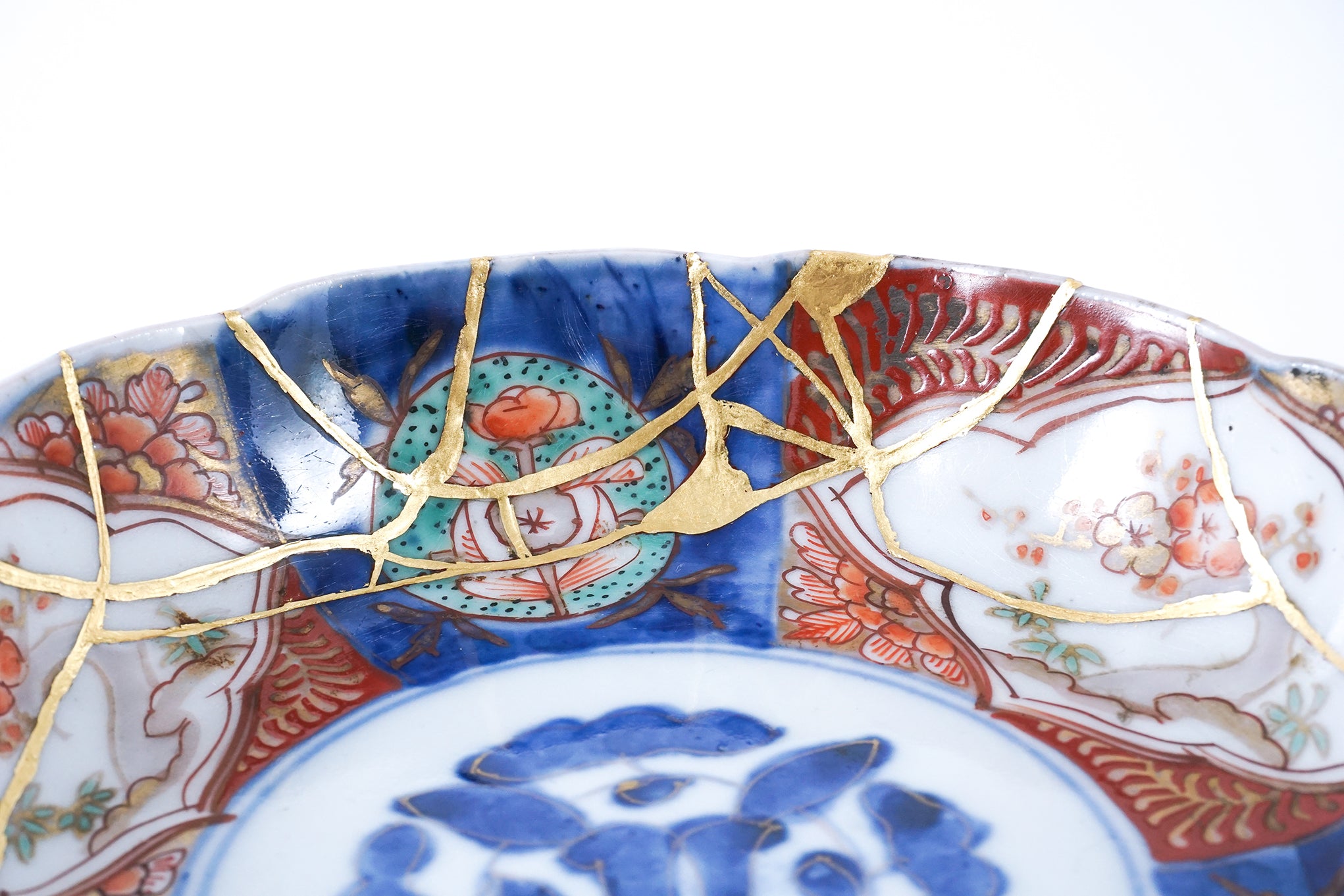 Close-up of a traditional Japanese porcelain plate repaired with gold Kintsugi technique, showing intricate floral design and detailed restoration work.