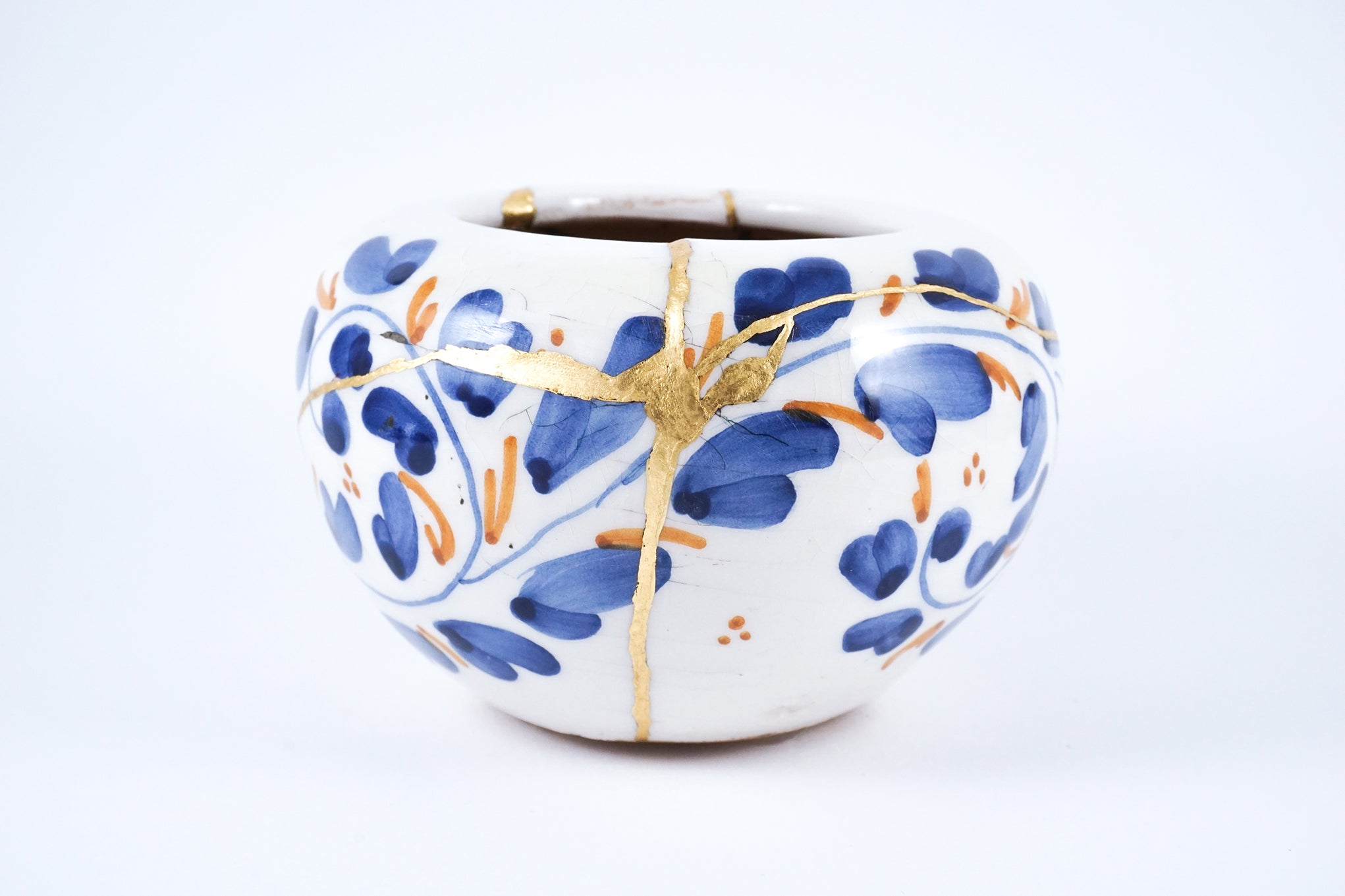 Small ceramic vase with blue and orange floral design, restored using traditional Japanese Kintsugi method with gold lacquer highlights.
