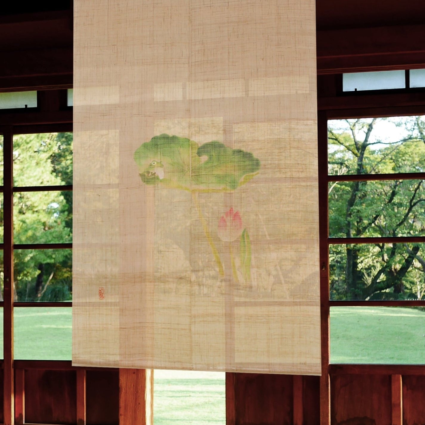 Lotus Pond noren curtain with frog and lotus design hanging in front of a sunlit Japanese window overlooking a garden.