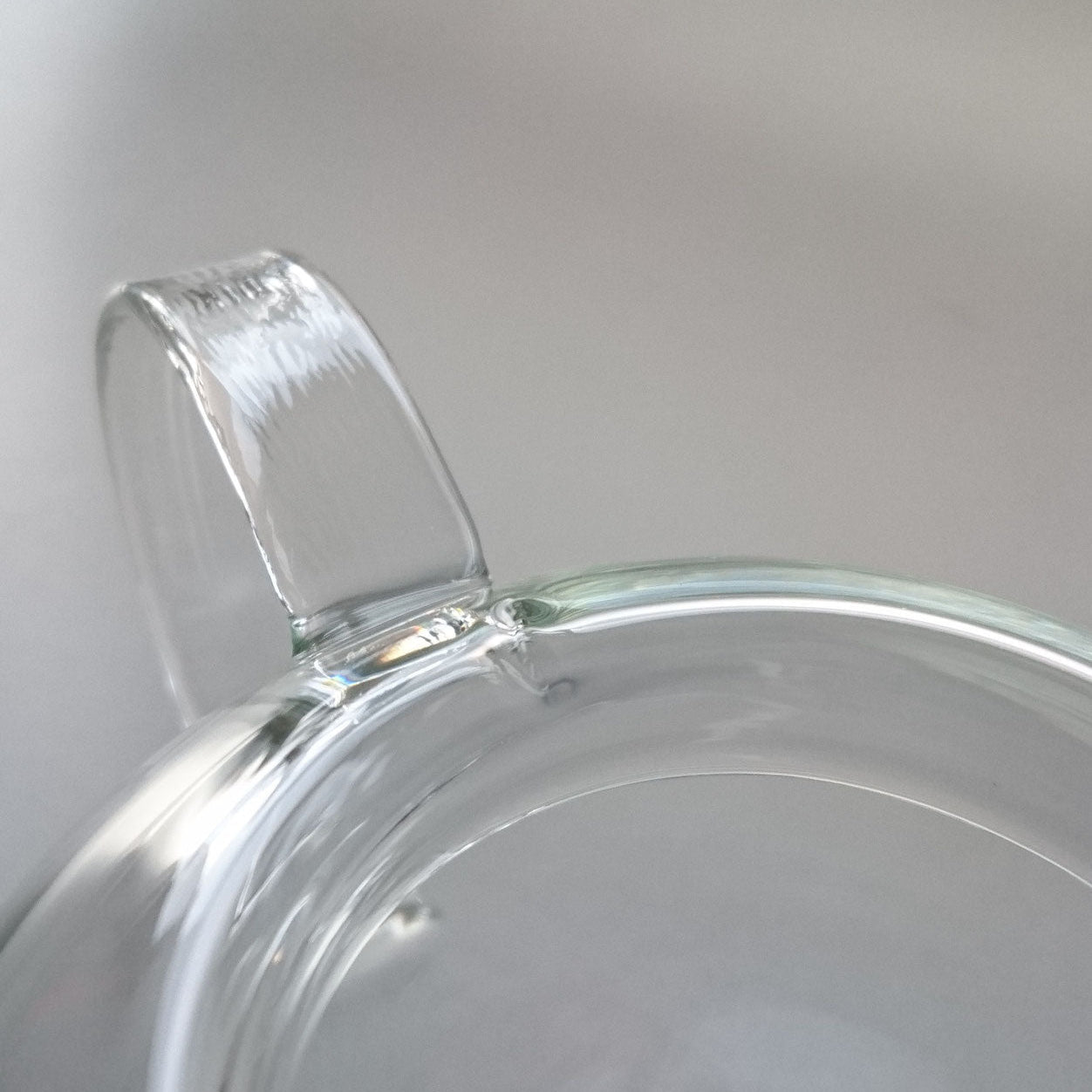 Close-up view of the Manmaru glass teapot handle, showcasing the smooth and seamless craftsmanship of the transparent borosilicate glass.